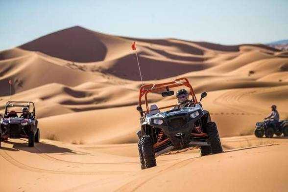Off-road orange and black dune buggy with drivers riding across golden sand dunes during Buggy Rental in Merzouga desert adventure
