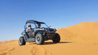 Off-road black and grey dune buggy with two riders wearing helmets on golden sand dunes under clear blue sky for Buggy Rental in Merzouga.