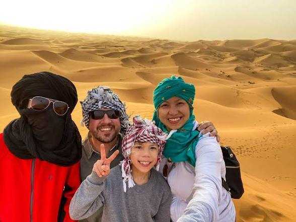 Camel Trekking group wearing colorful traditional headscarves smiling at desert dunes in Erg Chebbi Morocco