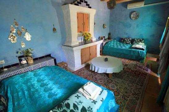 Traditional Moroccan bedroom with turquoise bedspreads, blue painted walls, patterned rugs, and decorative ceramic tiles, ideal for Camel Trekking in the Sahara Desert.