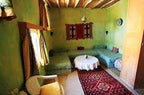 Traditional desert auberge interior with green walls, wooden ceiling beams, twin beds, patterned rug, and Camel Trekking in the Sahara Desert ambiance.