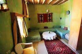 Traditional desert auberge interior with green walls, wooden ceiling beams, twin beds, patterned rug, and Camel Trekking in the Sahara Desert ambiance.