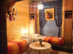 Traditional bedroom with two single beds featuring orange and red striped blankets, wooden furniture, and blue patterned curtains, ideal for a cozy stay during Camel Trekking in the Sahara Desert.