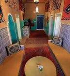 Traditional Moroccan interior with colorful mosaic tiles, patterned rugs, orange walls, and arched doorways featuring intricate designs for Camel Trekking in the Sahara Desert.