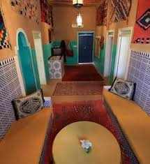 Traditional Moroccan interior with colorful mosaic tiles, patterned rugs, orange walls, and arched doorways featuring intricate designs for Camel Trekking in the Sahara Desert.