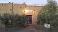 Auberge building with beige adobe walls, wooden door, greenery at entrance, lit sign reading Chez Julia supporting Camel Trekking in the Sahara Desert tours.