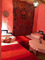 Traditional Moroccan twin beds with red bedding and a decorative tapestry on the wall, embodying the ambiance of Camel Trekking in the Sahara Desert.
