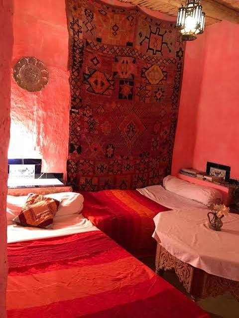 Traditional Moroccan twin beds with red bedding and a decorative tapestry on the wall, embodying the ambiance of Camel Trekking in the Sahara Desert.