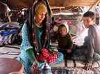 Woman and two children sitting on patterned rugs inside a traditional tent with woven textiles, part of Camel Trekking experience
