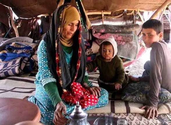 Woman and two children sitting on patterned rugs inside a traditional tent with woven textiles, part of Camel Trekking experience