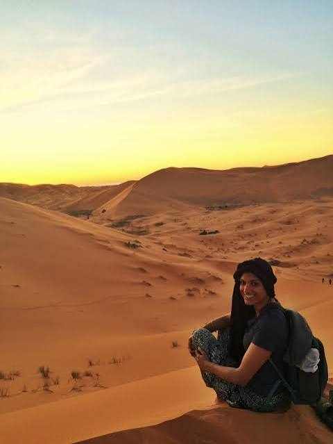 Camel trekking adventure featuring a woman sitting on golden sand dunes at sunset in Erg Chebbi desert