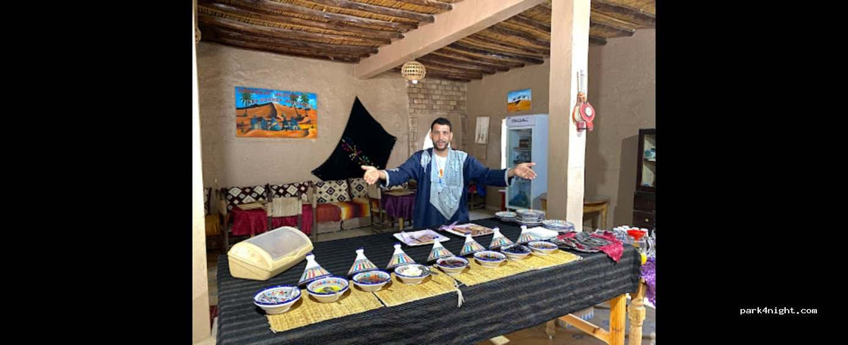 Indoor Moroccan dining table set with colorful tagine pots and bowls, decorated with traditional patterns at Campground les Roches Merzouga.
