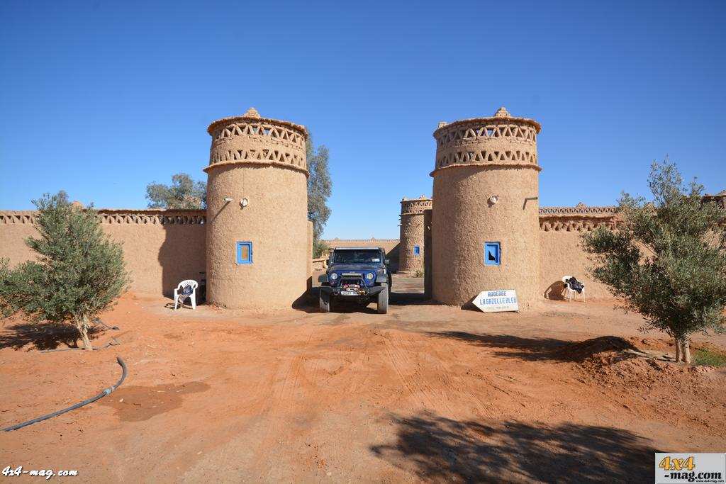 Camping La Gazelle Bleue entrance with traditional mud brick towers, blue window accents, and a black off-road vehicle in desert surroundings.