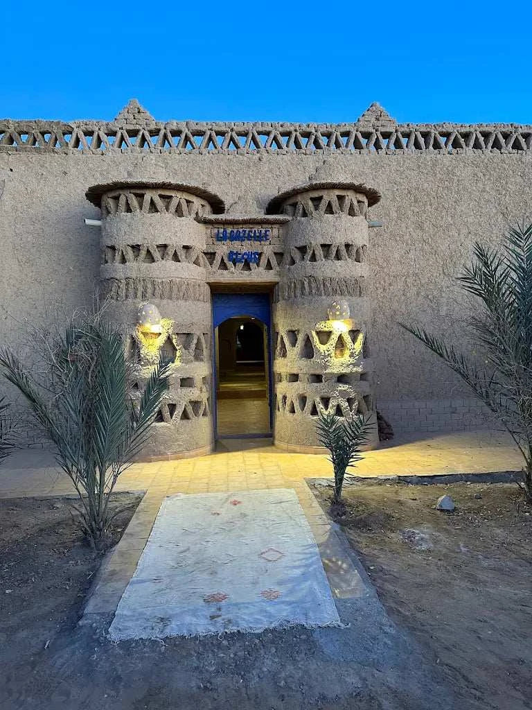 Camping La Gazelle Bleue entrance featuring traditional Moroccan mud architecture with decorative geometric patterns and blue signage at dusk