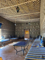 Camping La Gazelle Bleue interior lounge with blue and yellow striped cushions, patterned pillows, rustic brick walls, and decorative plates on wall