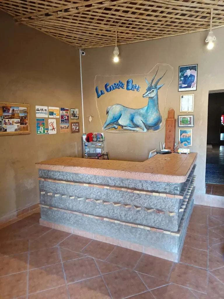 Reception desk with textured stone and wood design in a rustic room featuring a blue gazelle mural and framed artworks, representing Camping La Gazelle Bleue.