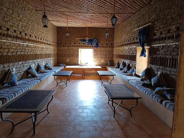 Traditional Moroccan indoor seating area with blue pattern cushions, brick walls, wooden ceiling, and hanging lanterns at Camping La Gazelle Bleue