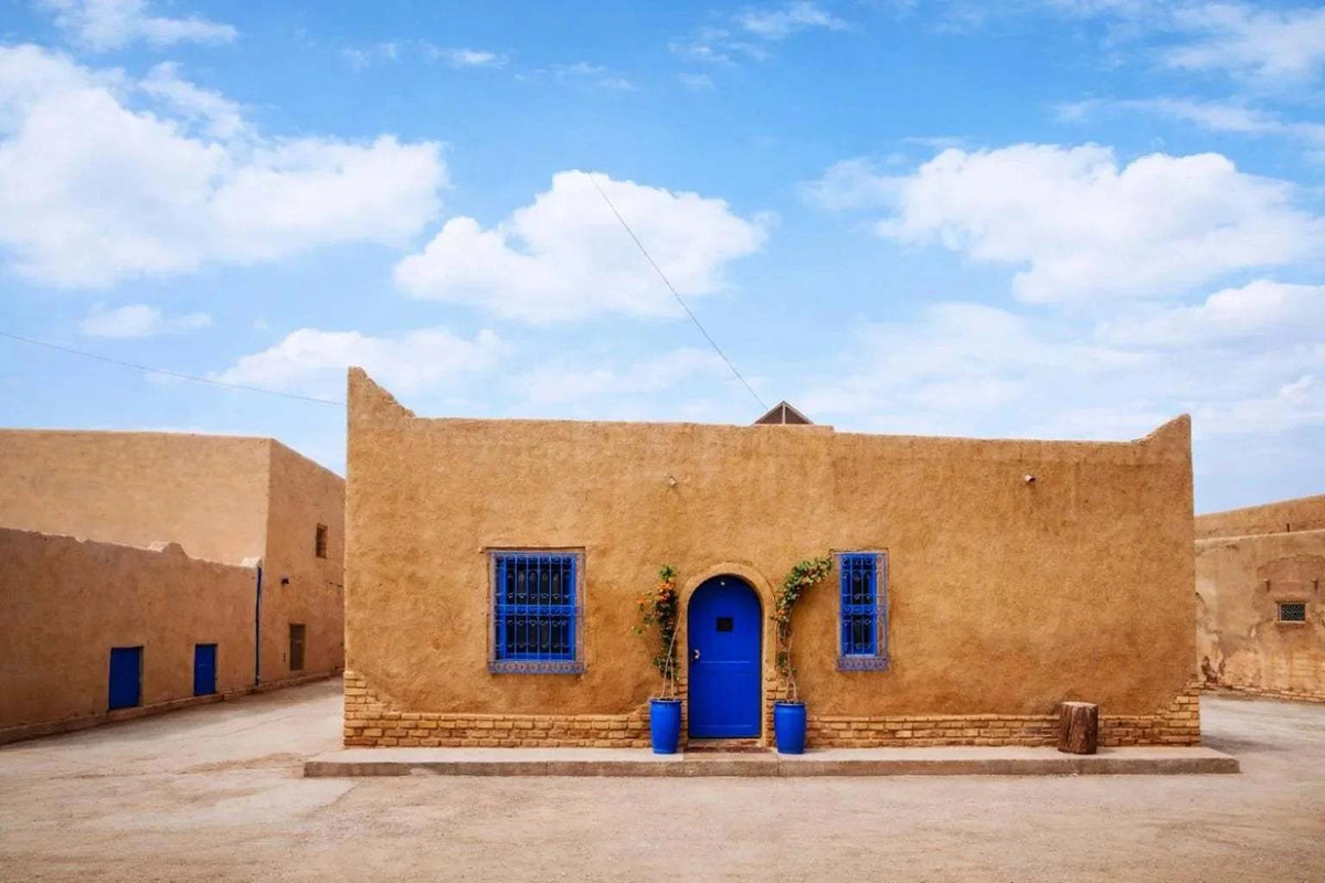 Casa Mona apartment showing a beige stucco exterior with vibrant blue door and window frames, adorned with potted plants.