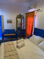 Chez Youssef Guesthouse bedroom with white linens, blue wooden bedframe and furniture, orange curtain, and air conditioning
