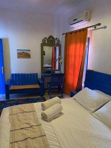 Chez Youssef Guesthouse bedroom with white linens, blue wooden bedframe and furniture, orange curtain, and air conditioning