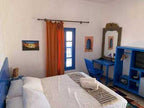 Chez Youssef Guesthouse bedroom with white walls, blue wooden furniture, orange curtain, and neatly made bed with white linens