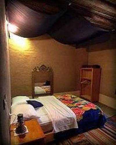 Chez Youssef Guesthouse cozy bedroom with earthy textured walls, colorful bedspread, wooden furniture and soft lighting