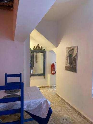 Chez Youssef Guesthouse interior featuring white walls, traditional blue wooden chairs, a mirror with ornate frame, and a wall-mounted fire extinguisher