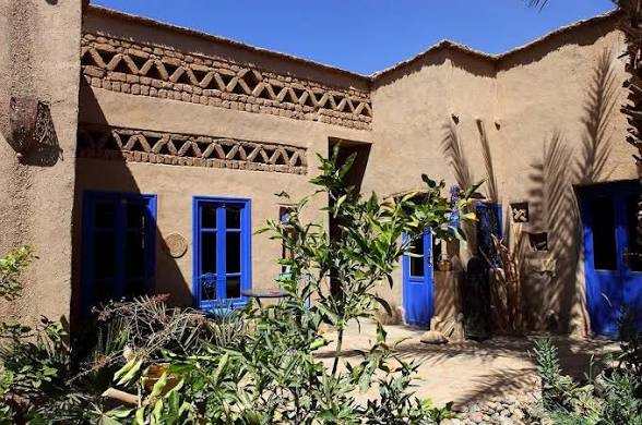 Traditional mud-brick guesthouse with bright blue wooden doors and windows, decorative geometric trim, and desert plants at Chez Youssef Guesthouse.