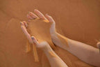 Hands holding and letting flow fine golden desert sand, creating a soft stream against a sandy background for Day Tour from Erfoud to Merzouga.