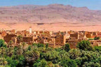 Day Tour from Fes to Merzouga featuring a desert village with brown adobe buildings surrounded by green palm trees and desert mountains
