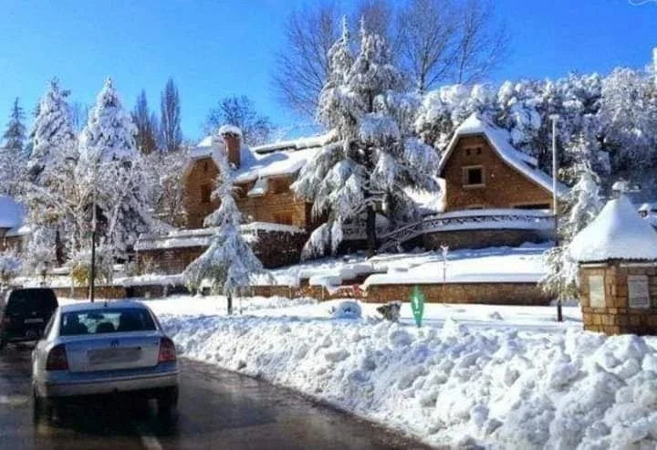 Day Tour from Merzouga to Fes featuring snow-covered rustic stone and wood houses with snow-laden pine trees under a clear blue sky