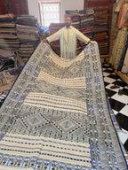 Moroccan man holding large beige and black patterned rug with geometric designs in a textile shop at Dépôt Nomade