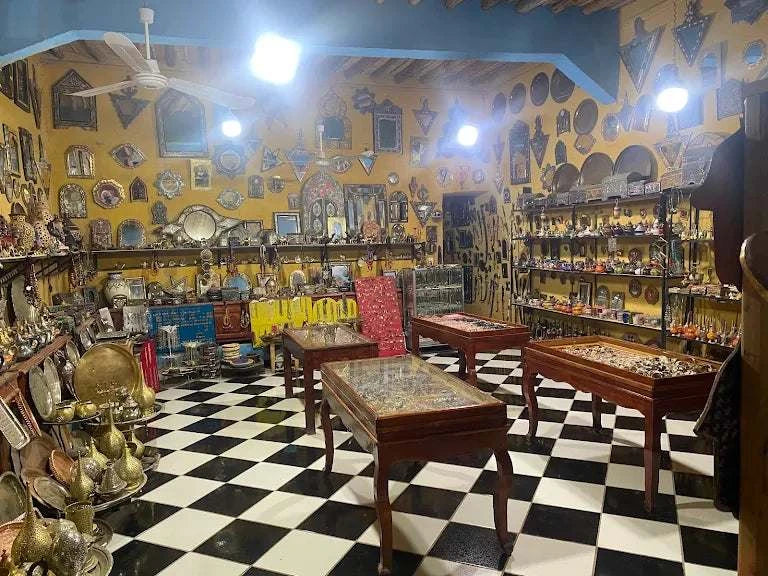 Moroccan-style shop interior with black and white checkered floor, yellow walls, wooden tables, and brass decorative items at Dépôt Nomade.
