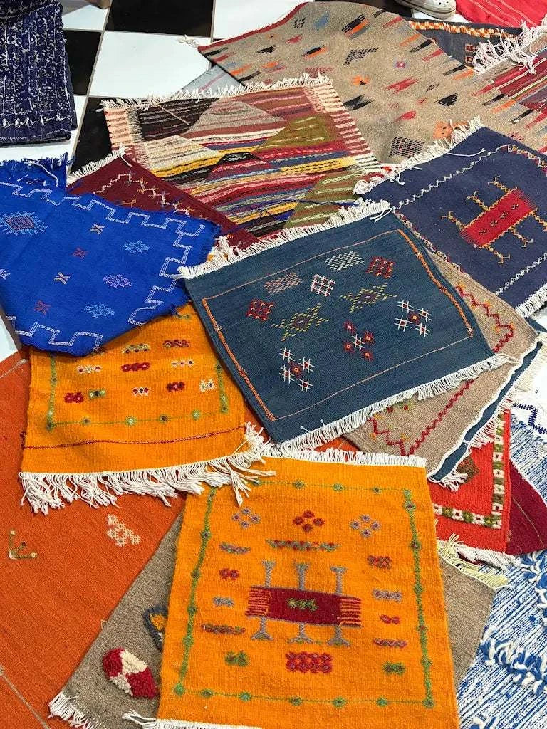 Colorful woven Moroccan rugs with traditional geometric patterns and fringe edges displayed in a layered arrangement, showcasing the vibrant artisan style found at Dépôt Nomade.