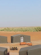 Desert Erg Chigaga Camp with traditional black Berber tents arranged around outdoor seating and tables against sandy dunes and clear sky