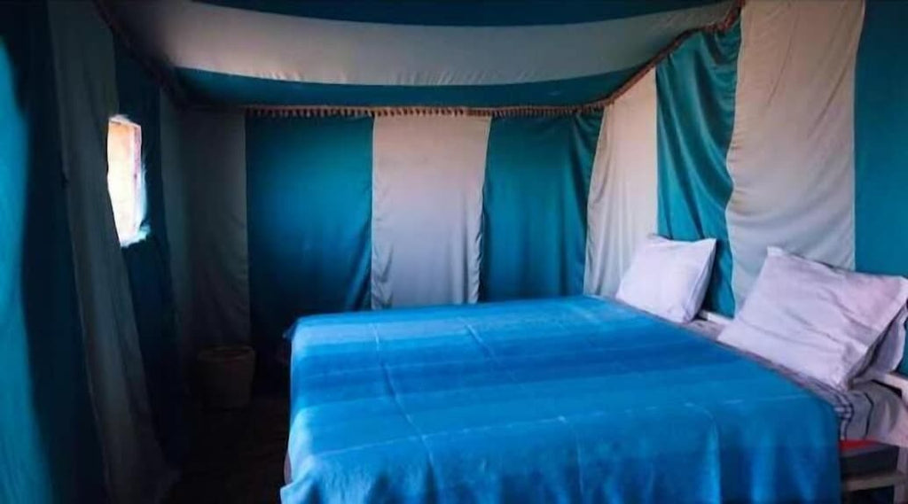 Desert Erg Chigaga Camp interior with a large double bed covered in blue bedding and blue-and-white striped tent walls