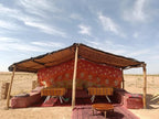 Desert Erg Chigaga Camp with open rustic shelter made of wood and reed, featuring red patterned fabric walls and low seating with cushions