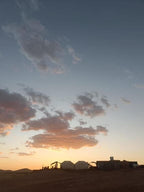 Desert Erg Chigaga Camp at sunset with traditional tan tents silhouetted against a colorful sky and scattered clouds