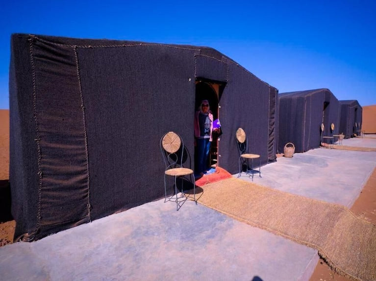 Desert Erg Chigaga Camp with traditional black fabric tents arranged in a row on concrete platforms under clear blue sky