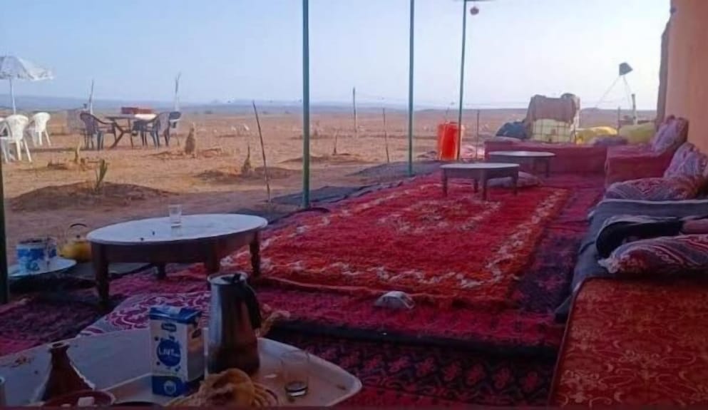 Desert Erg Chigaga Camp outdoor seating area with traditional red and patterned carpets, low tables, cushions, and panoramic desert view