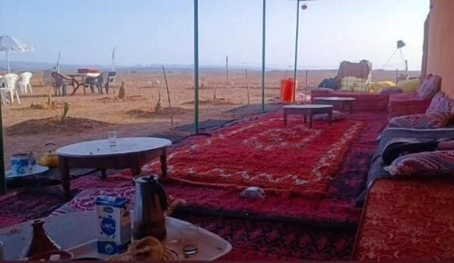 Desert Erg Chigaga Camp outdoor seating area with traditional red and patterned carpets, low tables, cushions, and panoramic desert view