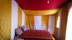 Desert Erg Chigaga Camp interior with traditional fabric walls featuring vertical yellow and white stripes and red ceiling, double bed with colorful striped bedding and patterned pillows