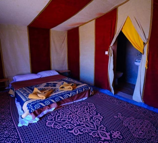 Desert Erg Chigaga Camp traditional tent interior with red and beige striped fabric walls, carpeted floor, double bed with patterned blankets