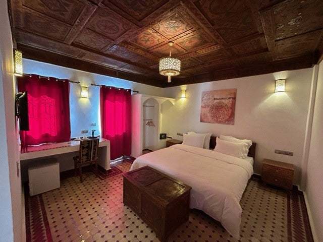 Desert Villa Boutique Hotel bedroom with white bedding, red curtains, patterned tile floor, and ornate wooden ceiling