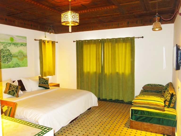 Desert Villa Boutique Hotel bedroom with white bed linens, green curtains, traditional wooden ceiling, green patterned cushions, and wall art