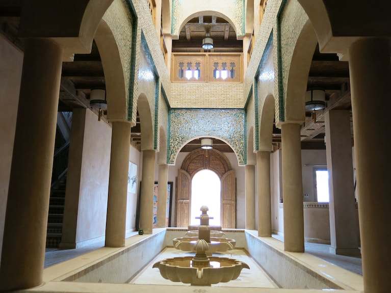 Desert Villa Boutique Hotel interior showing beige columns and arches with intricate blue mosaic tilework above a central reflective water fountain