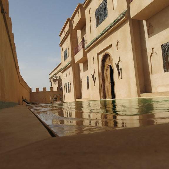 Desert Villa Boutique Hotel with beige stucco walls, arched wooden door, ornate metal window grilles, and a reflective pool in front