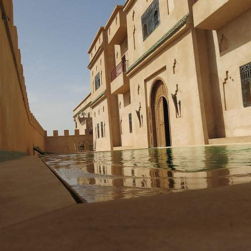 Desert Villa Boutique Hotel with beige stucco walls, arched wooden door, ornate metal window grilles, and a reflective pool in front