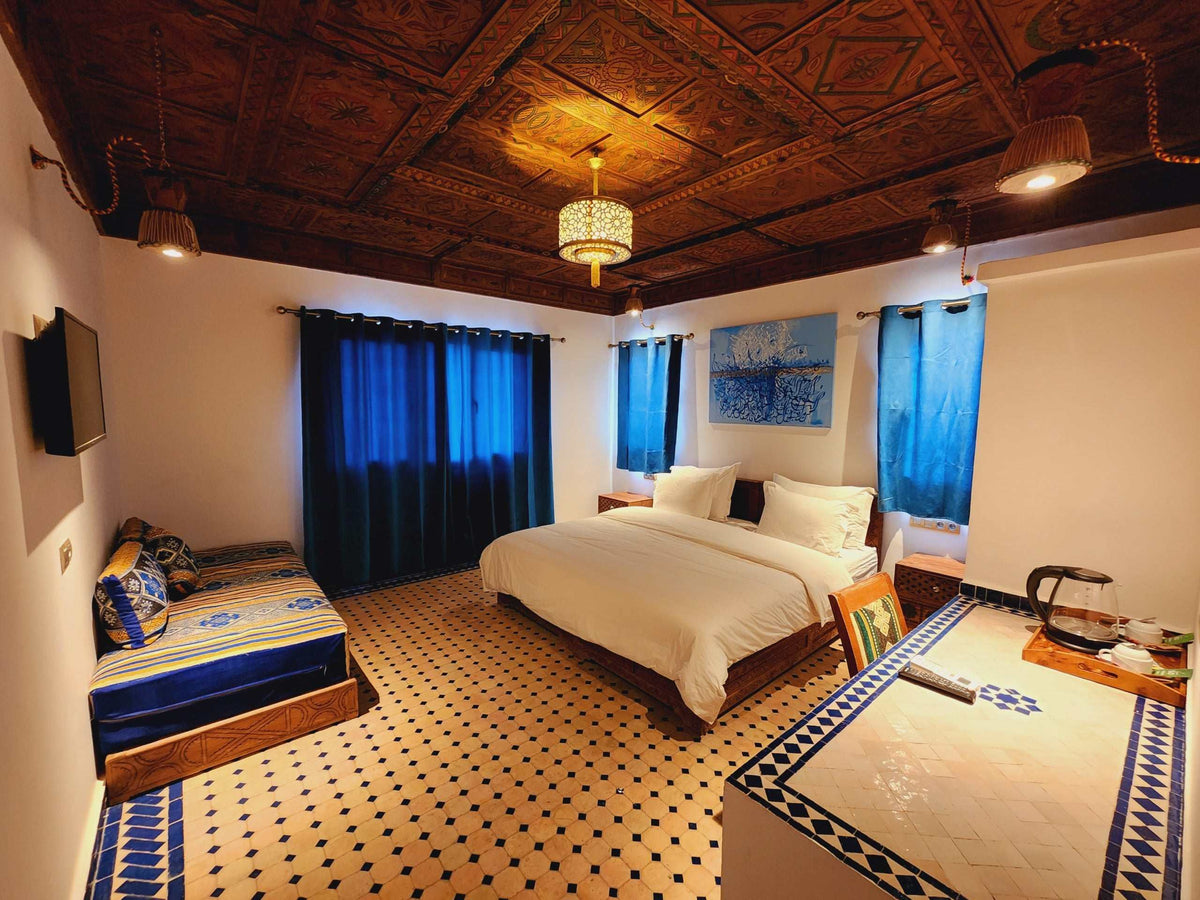 Desert Villa Boutique Hotel bedroom with blue curtains, patterned tiles, wooden ceiling, double bed, and seating area