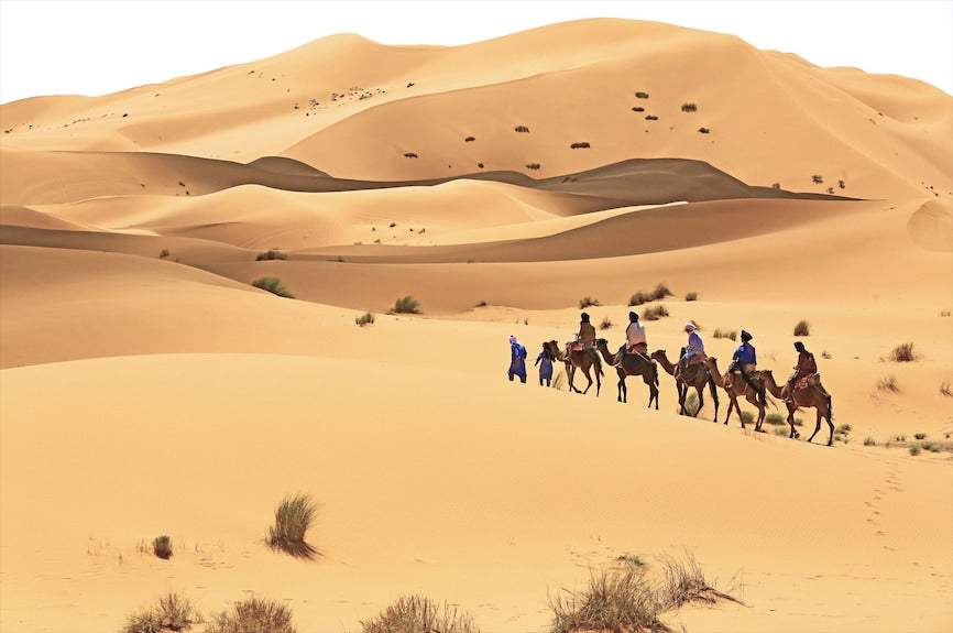 Desert Villa Boutique Hotel camel trek with travelers riding camels across golden sand dunes in the Sahara desert landscape